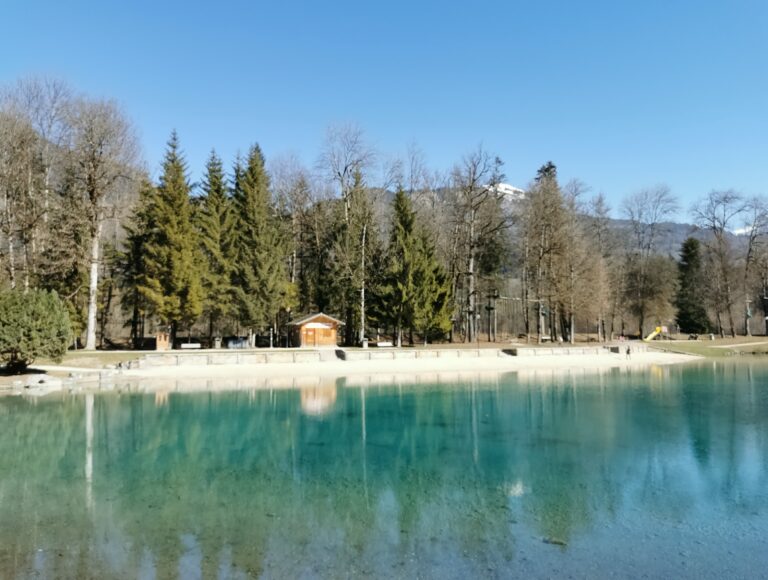 Famille au bord du Lac Bleu de Morillon par beau temps, avec eau calme, prairie et montagnes en arrière-plan.
